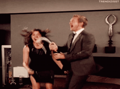 A Man In A Suit Is Holding A Woman In A Black Dress Who Is Laughing GIF