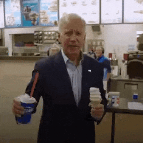 A Man In A Suit Is Holding An Ice Cream Cone And A Cup With A Straw . GIF