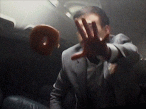 A Man In A Suit Is Holding His Hand Up In Front Of A Doughnut GIF
