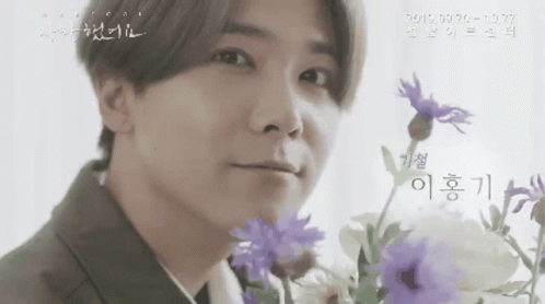 A Man In A Suit Is Holding Purple Flowers In Front Of His Face .. GIF