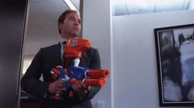 A Man In A Suit Is Holding Two Nerf Guns . GIF