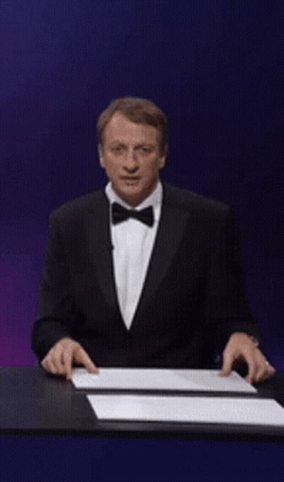 A Man In A Suit Is Holding Up A Sign That Says Tony Hawk GIF