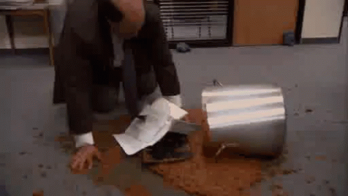 A Man In A Suit Is Kneeling Down On The Floor Next To A Bucket Of Coffee . GIF