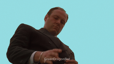 A Man In A Suit Is Kneeling In Front Of A Fence With A Green Dragonbot Watermark GIF