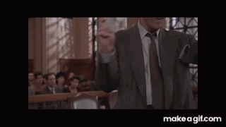 A Man In A Suit Is Laughing In A Courtroom While Holding Something In His Hands . GIF