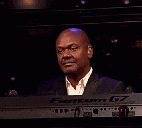 A Man In A Suit Is Laughing While Playing A Keyboard In A Dark Room . GIF