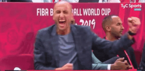 A Man In A Suit Is Laughing While Sitting In A Stadium . GIF