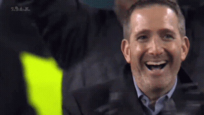 A Man In A Suit Is Laughing While Sitting In The Stands . GIF
