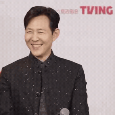A Man In A Suit Is Laughing With His Eyes Closed And His Hands In The Air . GIF