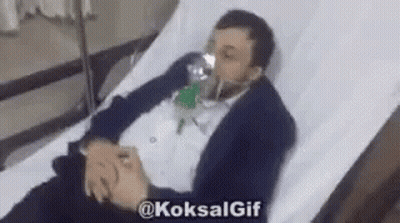 A Man In A Suit Is Laying In A Hospital Bed With An Oxygen Mask On His Face . GIF