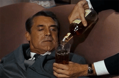 A Man In A Suit Is Laying On A Couch While Someone Pours A Drink Into A Glass GIF