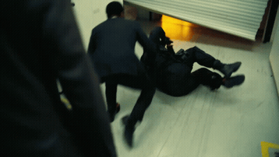 A Man In A Suit Is Laying On The Floor While Another Man Stands Behind Him GIF