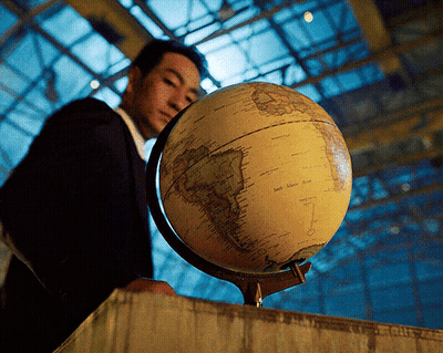 A Man In A Suit Is Looking At A Globe With The Words South America On It GIF