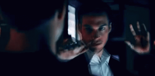 A Man In A Suit Is Looking At Himself In The Mirror . GIF