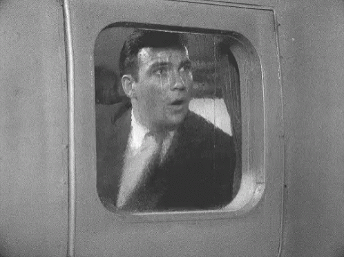 A Man In A Suit Is Looking Out Of A Window GIF