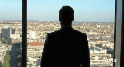 A Man In A Suit Is Looking Out Of A Window With Netflix Written On The Bottom GIF