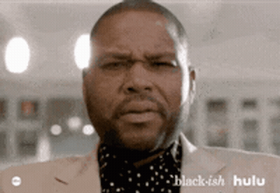 A Man In A Suit Is Making A Funny Face . GIF
