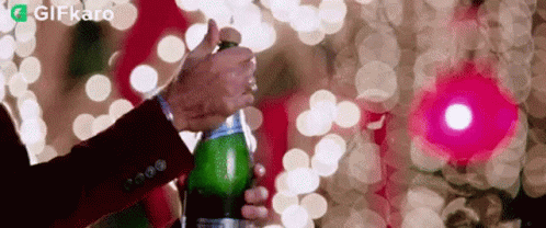 A Man In A Suit Is Opening A Bottle Of Champagne In Front Of A Christmas Tree . GIF