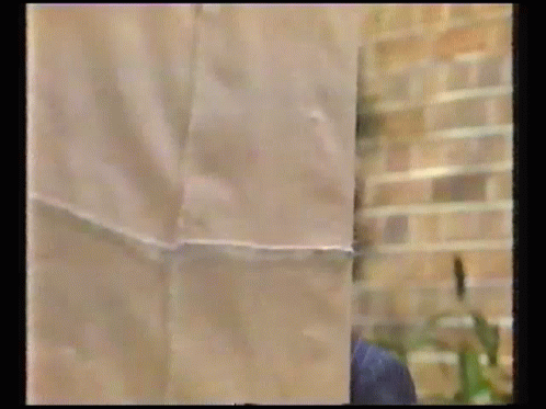 A Man In A Suit Is Peeking Out From Behind A Piece Of Paper GIF