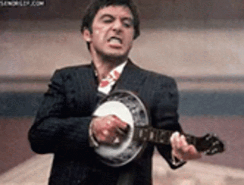 A Man In A Suit Is Playing A Banjo While Making A Funny Face . GIF
