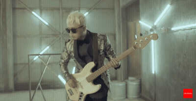 A Man In A Suit Is Playing A Guitar In A Room With Lights Behind Him GIF