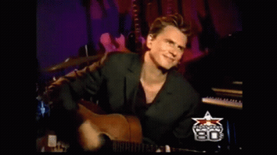 A Man In A Suit Is Playing A Guitar In Front Of A Sign That Says ' 80 ' On It GIF