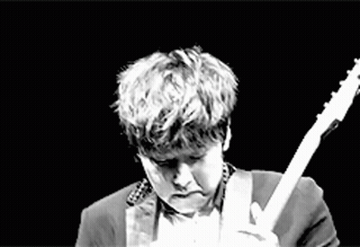 A Man In A Suit Is Playing An Electric Guitar On A Stage In A Black And White Photo . GIF