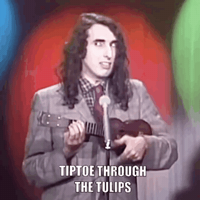 A Man In A Suit Is Playing An Ukulele In Front Of A Microphone . GIF