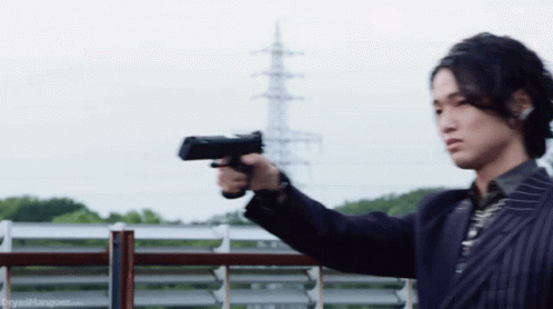 A Man In A Suit Is Pointing A Gun At A Fence . GIF