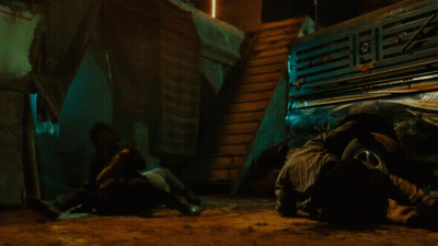 A Man In A Suit Is Pointing A Gun At Another Man In A Mask GIF