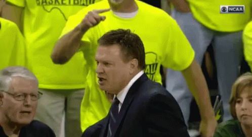 A Man In A Suit Is Pointing At Someone Wearing A Ncaa Shirt GIF
