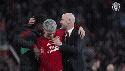 A Man In A Suit Is Putting His Hand On A Man In A Red Teamviewer Jersey GIF