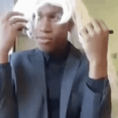 A Man In A Suit Is Putting On A Wig . GIF