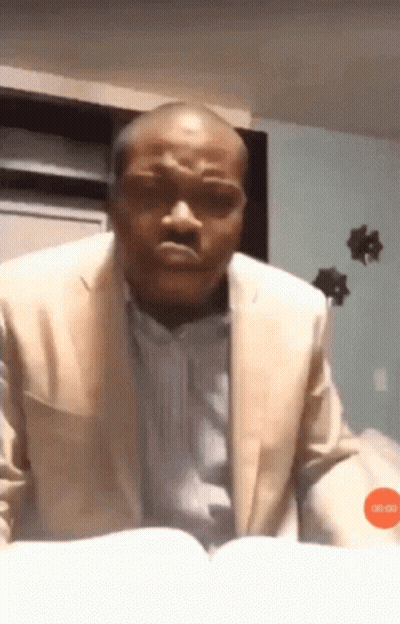 A Man In A Suit Is Reading A Book And Making A Face GIF