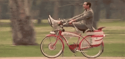 A Man In A Suit Is Riding A Bicycle With His Feet Up In A Park . GIF