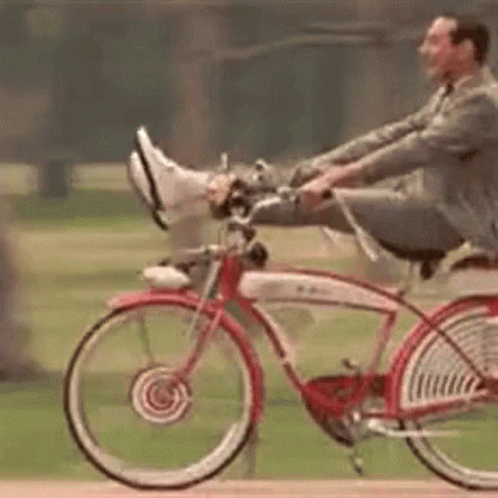 A Man In A Suit Is Riding A Red Bicycle With His Feet Up . GIF