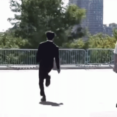 A Man In A Suit Is Running Down A Street Holding A Briefcase . GIF