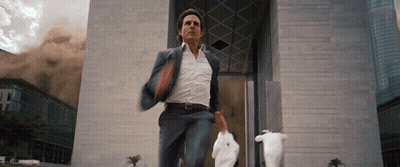 A Man In A Suit Is Running In Front Of A Building GIF