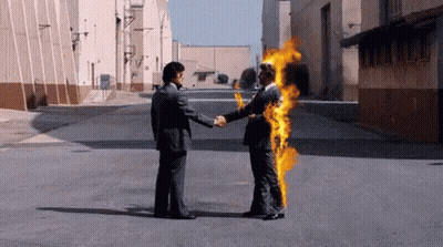 A Man In A Suit Is Shaking Hands With Another Man In A Suit Who Is On Fire . GIF