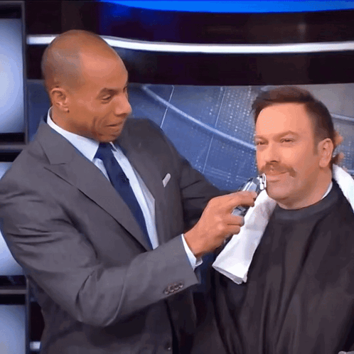 A Man In A Suit Is Shaving Another Man 'S Face With A Razor GIF