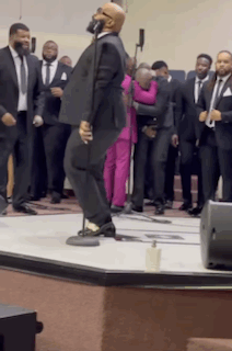 A Man In A Suit Is Singing Into A Microphone In Front Of A Crowd Of Men In Suits GIF