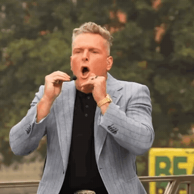 A Man In A Suit Is Singing Into A Microphone In Front Of A Yellow Sign That Says Re GIF