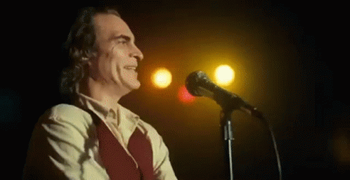 A Man In A Suit Is Singing Into A Microphone On A Stage . GIF