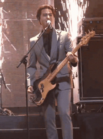 A Man In A Suit Is Singing Into A Microphone While Playing A Bass Guitar GIF