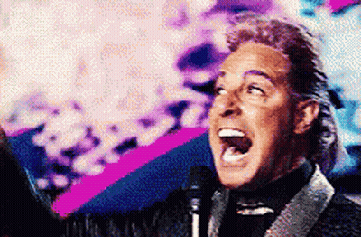 A Man In A Suit Is Singing Into A Microphone With His Mouth Open GIF