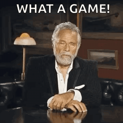 A Man In A Suit Is Sitting At A Table Covering His Face With His Hand And Making A Funny Face . GIF