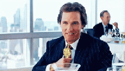 A Man In A Suit Is Sitting At A Table Holding A Trophy GIF