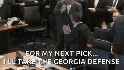 A Man In A Suit Is Sitting At A Table In Front Of A Group Of People Applauding . GIF