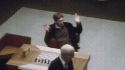 A Man In A Suit Is Sitting At A Table With A Chess Board In Front Of Him . GIF