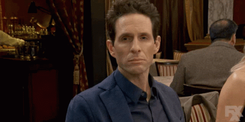 A Man In A Suit Is Sitting At A Table With A Fx Logo In The Corner GIF
